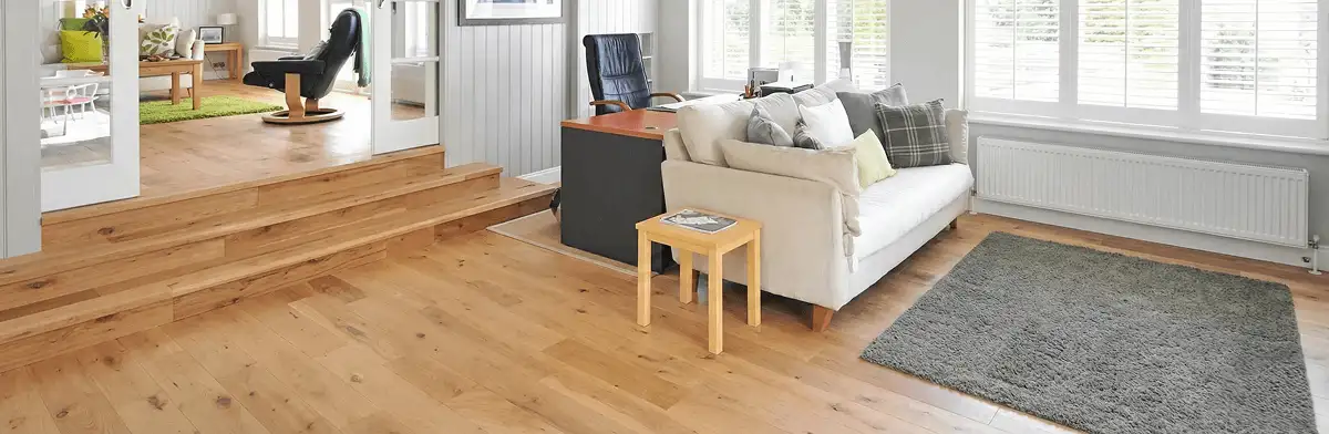 A modern living room with professionally installed laminate flooring, a beige sofa, a small side table, a gray rug, and large windows with white shutters in Bradenton, FL